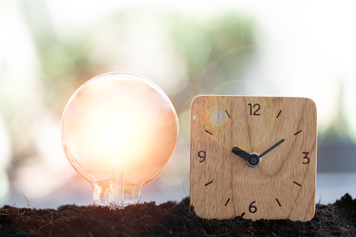 Light bulb and wood clock on the soil. New ideas, time to saving energy concept. Save the world concept, ecology system concept