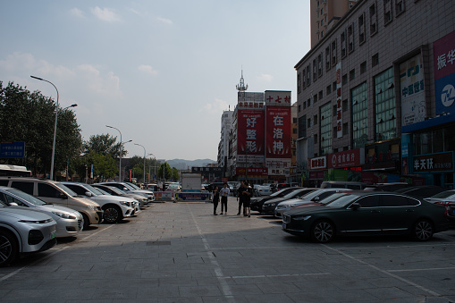 xingfu middle road, Yantai, shandong, china - august 19, 2023 : rows of cars parked in opem parling lot at the side walk space