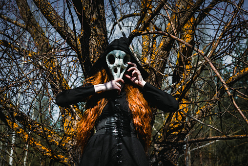 Woman in a black robe with a skull and a book in a dark forest. A mystical portrait of a witch. The concept of witchcraft and occultism.