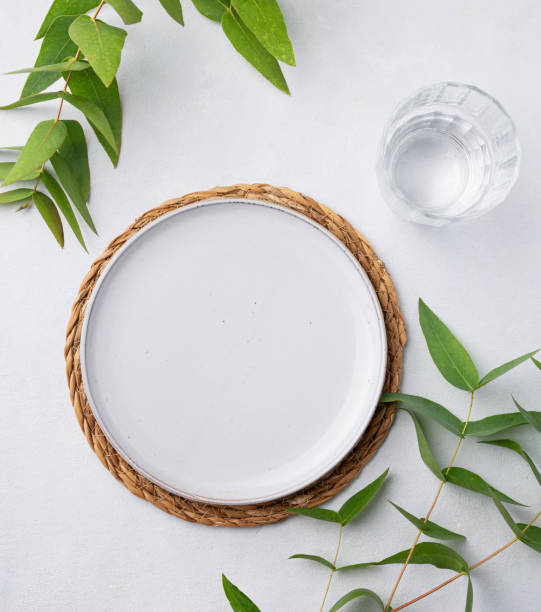 istock Table setting with a blue plate and a glass on a straw napkin with eucalyptus branches on a light background. Spring concept with cutlery. 1625151088
