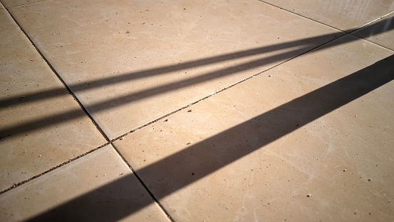 The beam of sunlight onto an object forms a black shadow with three thick lines on the surface of the tiled floor