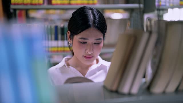 Asian women Students at rows of bookshelves searching for class assignments and exam preparations read books in the university library.