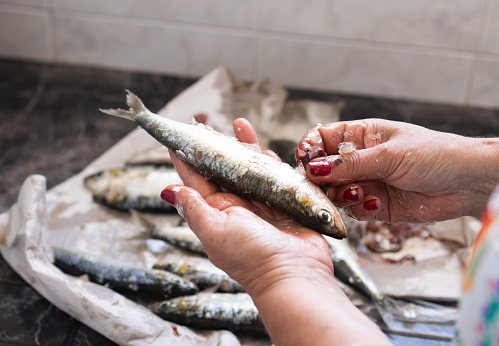 woman cleaning scales from a sardine by hand in the home kitchen. fish concept and prepare for cooking.