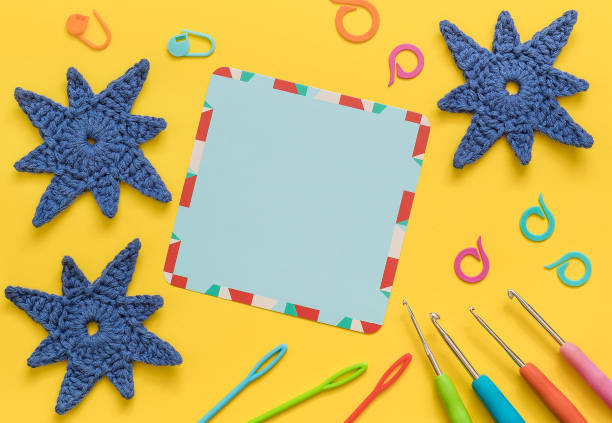 Empty blue card with crochet tools, crochet blue snowflakes on a yellow background. Top view. Copy space.