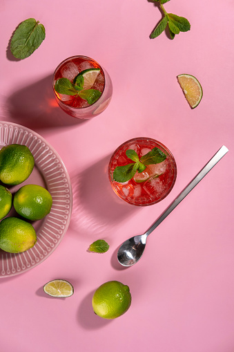 Strawberry mojito. Cocktail with rum, mint, lime and ice in a glass on a pink background. Homemade beverage.