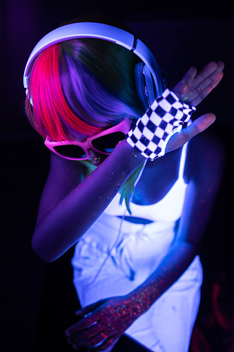 Portrait of a young DJ girl is hiding her face under a UV light