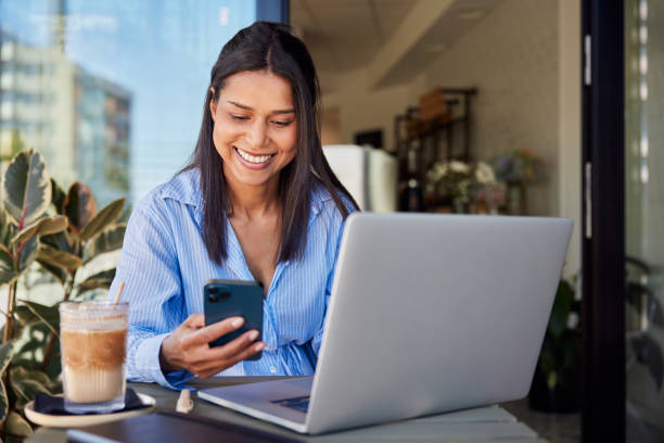 Smiling businesswoman using cellphone and laptop while in cafe