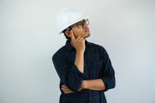 young asian male engineer wearing white hard hat touch the temples thinking for construction work isolated on white background, copy space. - pusing imagens e fotografias de stock
