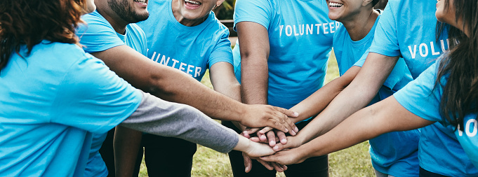 Feliz grupo de voluntarios apilando manos celebrando juntos al aire libre - Concepto de trabajo en equipo y apoyo de caridad - Enfoque en las caras traseras photo
