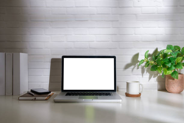 istock Laptop computer, coffee cup and book on white table against brick wall. Blank screen for your advertise text. 1625320250