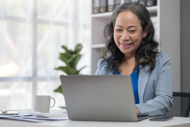 istock Aged businesswoman reading information on paperwork and using laptop working on desk. 1625327213