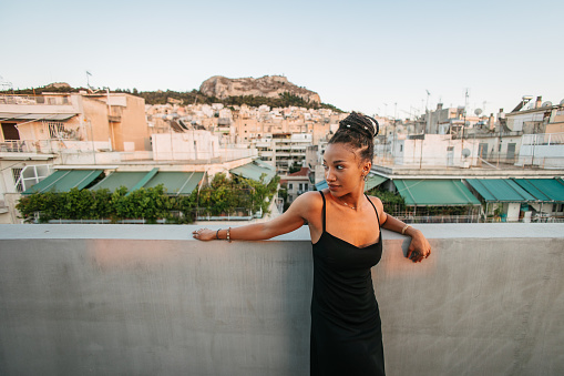 Side view of a young African woman with braids on a building rooftop posing by the wall at sunset