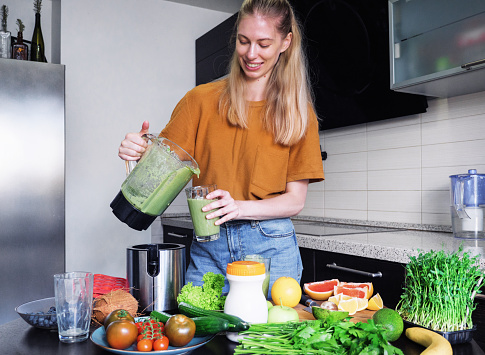 Beautiful young woman preparing a healthy smoothie with protein in a blender