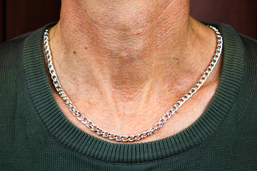 Man with a silver chain around his neck. Men's jewelry, silver chain. A man in a jumper with a chain around his neck.