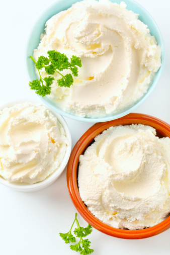 soft cream cheese in various ceramic bowls on a white background
