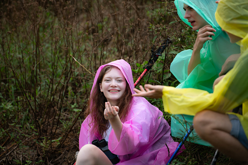 Group of friends in raincoat with backpacks hiking in the forest, Sit and shelter from the rain