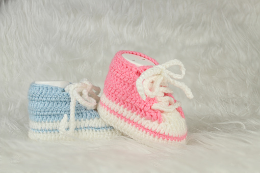 Gender party concept idea. Booties for baby girl or boy for first step. Knitted pink and blue booties on white fluffy blanket.