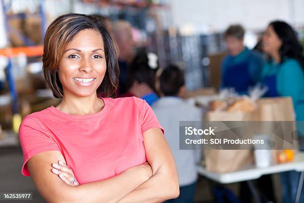 Young Woman Volunteer At A Food Bank Facility Stock Photo - Download Image Now - Arms Crossed, Charity and Relief Work, A Helping Hand