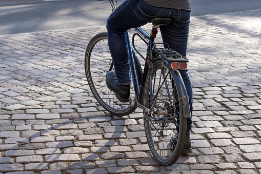 man with black city bike stands on cobblestones