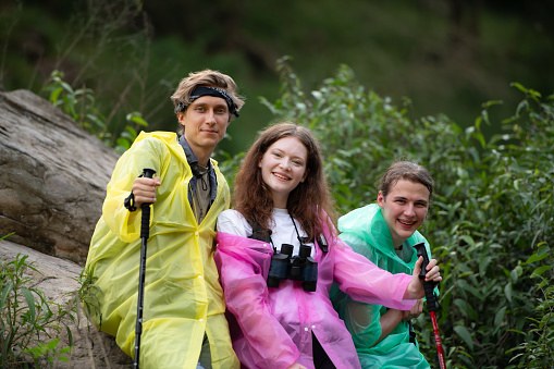 Group of friends in raincoats with backpacks on a hike in the forest, Prepare to hiking after the rain has stopped.