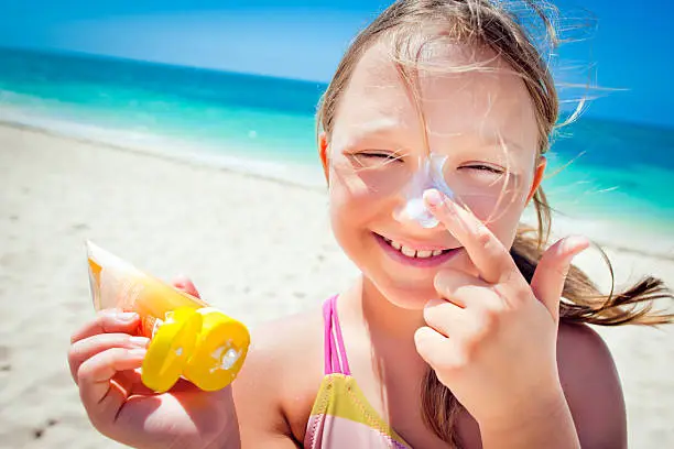Little girl applying suntan lotion on the beach