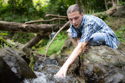 Hiker in the jungle playing with water in a stream in the forest.