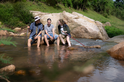 Group of friends sitting on the rock in the middle of the river. Rest during the hiking in the forest.