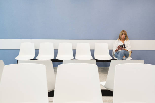 Senior woman using mobile phone in waiting room. Woman in the hospital waiting room, sitting alone and using a smartphone.