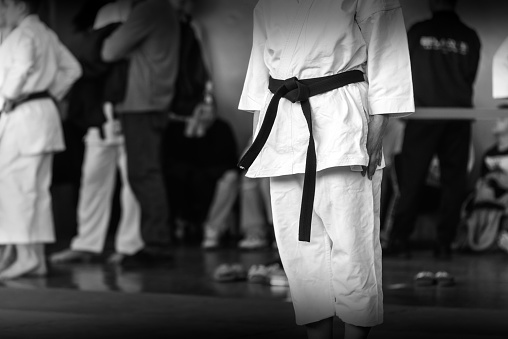 A martial arts athlete in a white kimano with a black belt is preparing for a fight. Black and white photo with motion blur effect.