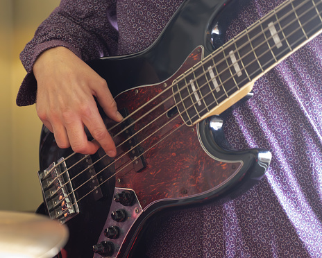 close up of a man in purple shirt playing a electric bass guitar