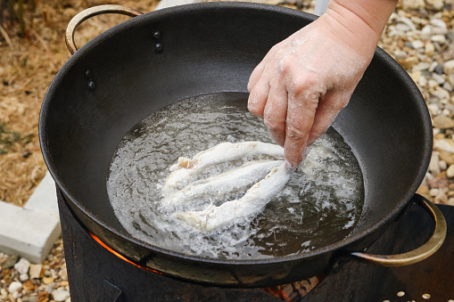 Roasting capelin in a cast iron pan (Kazan) on fire. Sardine fried in oil with crispy breading. Small fish fry in a pan. Small crispy fish are fried in oil. Shallow depth of field
