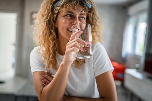 one adult caucasian woman sit at home hold glass of water happy smile
