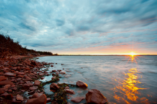 Sun drops over the horizon with some flare along the rugged north shore of Prince Rdward Island