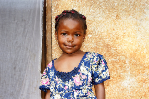 Portrait of a cute and sweet little black African girl, smiling but looking a bit shy, posing in front of her house. More people at: http://tonytremblay.com/sylvie/people.jpg