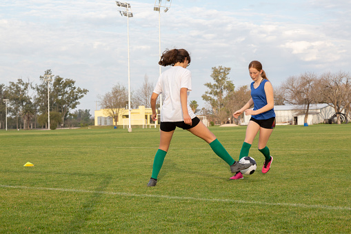 Teenage soccer player passing her opponents while running with a ball on playing filed.