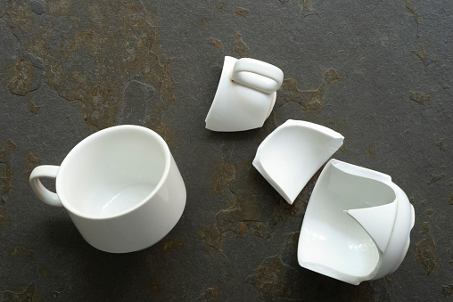 Whole white cup and other broken over a stone table in the kitchen