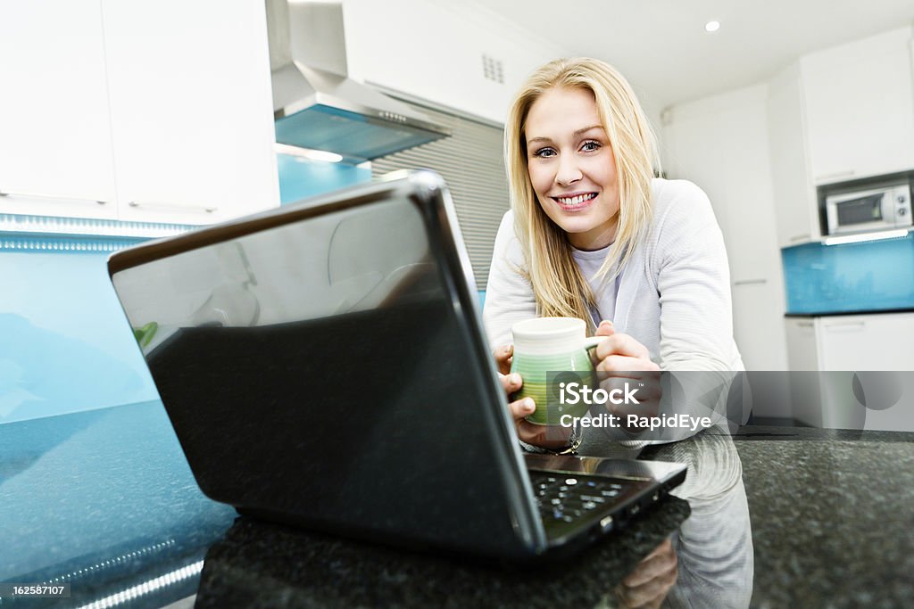 Jeune femme avec ordinateur portable et tasse de café dans la cuisine moderne - Photo de Cuisine libre de droits