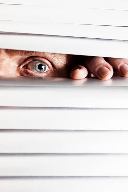 istock Man's worried-looking eye peeps out through closed venetian blinds 162587154