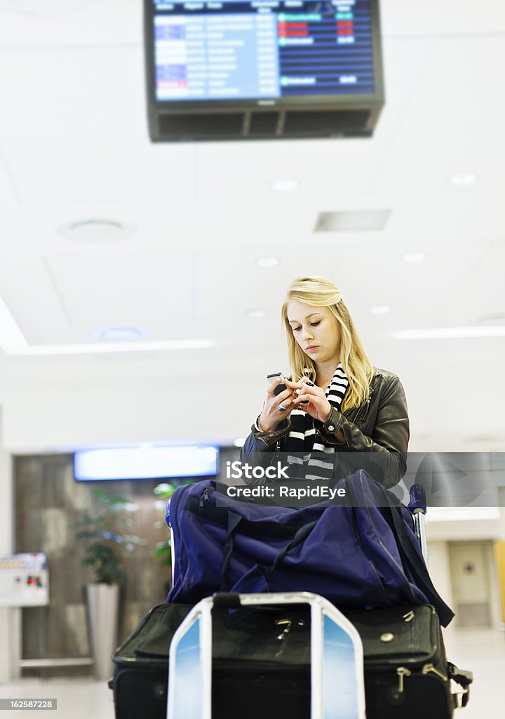 Grave jovem viajante no aeroporto com bagagem envia uma mensagem de texto - Foto de stock de Aeroporto royalty-free