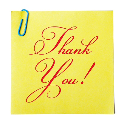 'Thank you' written on a yellow paper note held with a paper clip. Isolated on a white background.