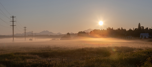 Fog over the fields, mountains in background on a summer morning in the Lowel River Valley outside Snohomish and Everett Washington