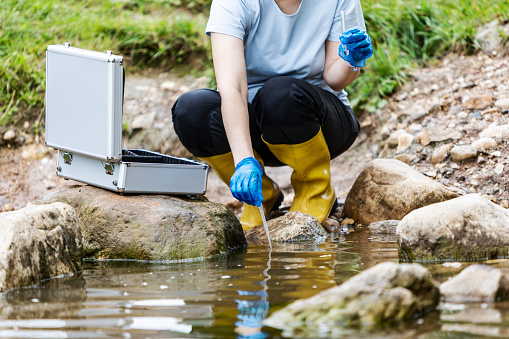 Mature woman collected river water sample for analysis in a test tube and recorded the experimental results in the tablet. Environmental research.