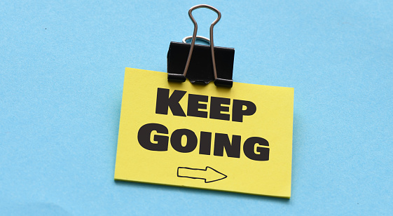 keep going handwriting on a sticky note, motivation or determination concept.