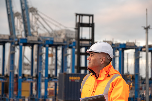 A male port worker looking into the distance with cranes in the background