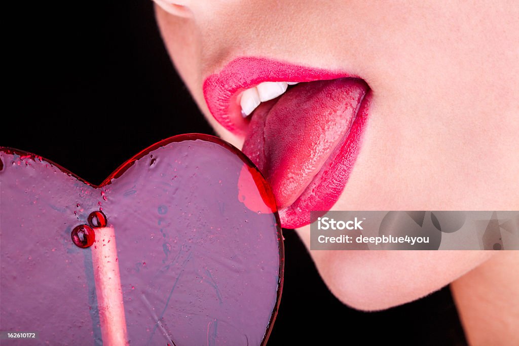 Girl licks corazón piruleta sobre fondo negro - Foto de stock de Labios - Boca humana libre de derechos