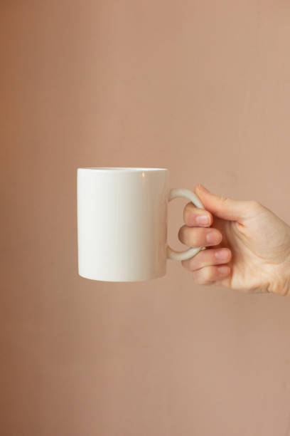 istock mockup ceramic white coffe cup or mug in female hands on white background with copy space. Blank template for your design, branding, business. 1626127132