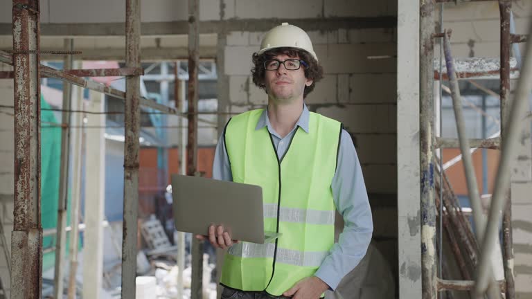 Caucasian white and black civil engineers with safety suit and helmet inspecting construction of building and checking blueprint or drawing.Architecture professional,worker,labor day concept.