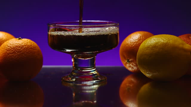 Whisky is poured into the glass on a colorful wall background. Stock clip. Oranges lying on a table at the night club