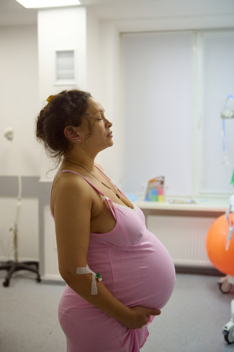 Pregnant woman, birthing mother in hospital ward, ready to delivery a baby, holding belly and practicing breathing exercises to induce an easy delivery. Childbirth. Obstetrics and gynecology concept