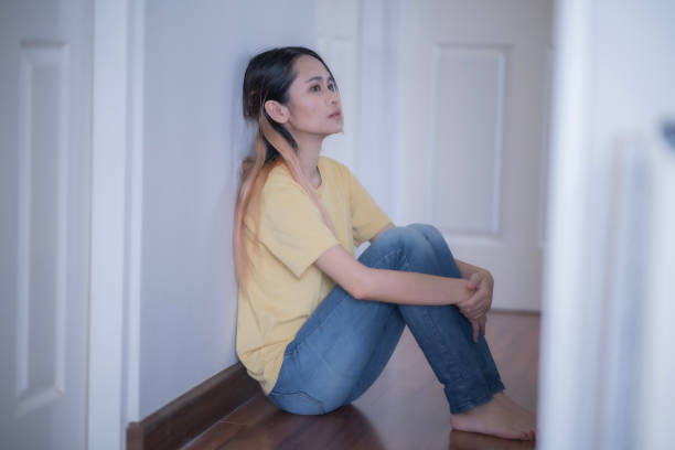 istock Young Asian woman sitting at broken wall embraces her knee with depression disease expression. 1626571862